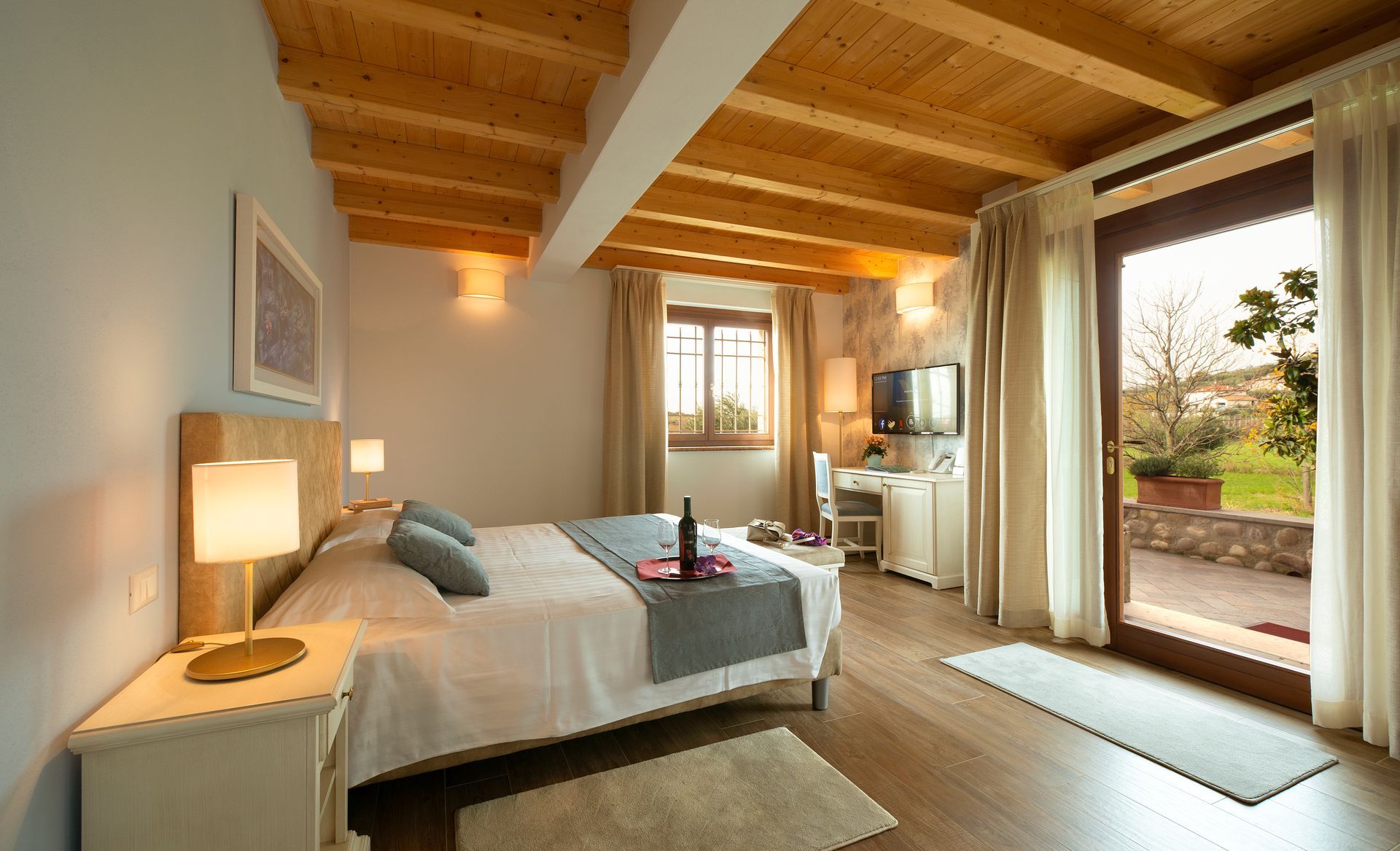 Luminosa camera da letto con soffitto in legno, due letti singoli, lampada a luce calda e porte scorrevoli che conducono a un patio con giardino.