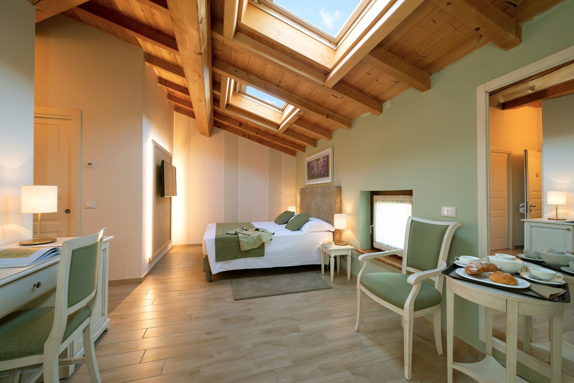 Luminosa camera da letto mansardata con travi in ​​legno a vista, lucernari e due scrivanie vicino alla finestra.