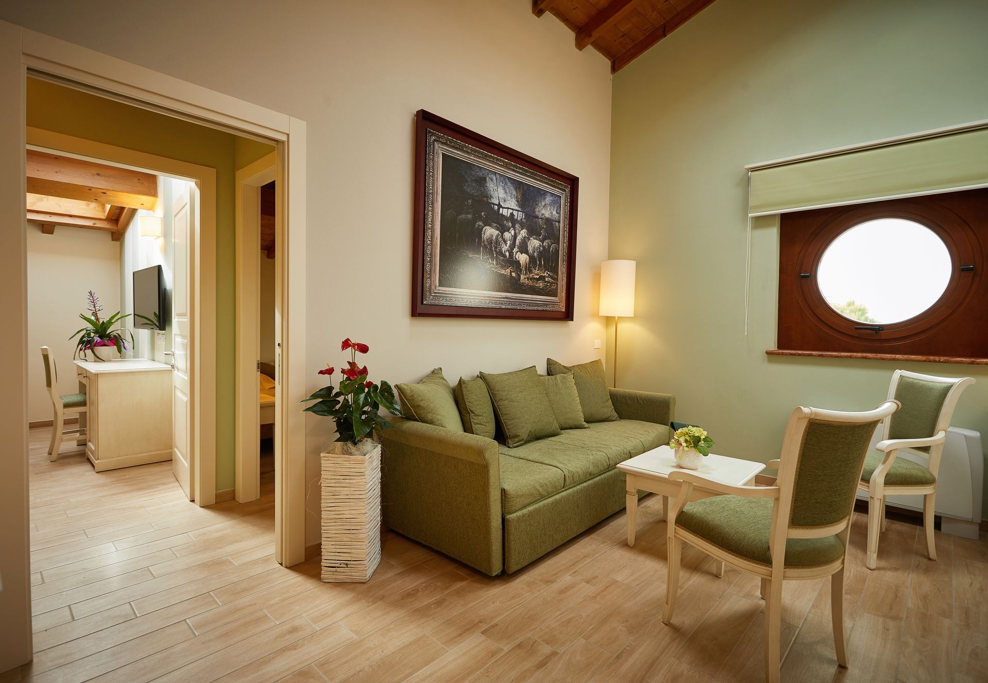 Accogliente soggiorno con divano verde, poltrone, lampada e porta aperta su una cucina luminosa.