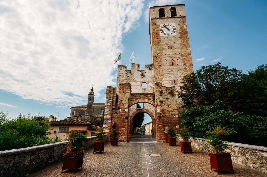Torre di pietra con orologio e ingresso ad arco su un sentiero, sotto un cielo nuvoloso