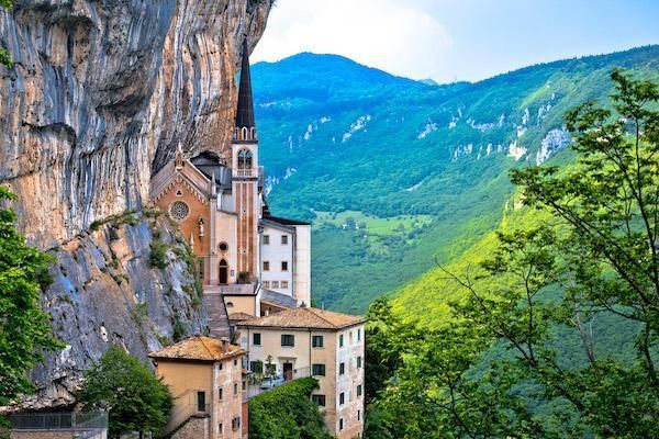 Monastero a picco sulla scogliera, affacciato su una verde vallata di montagna sotto un cielo azzurro brillante.