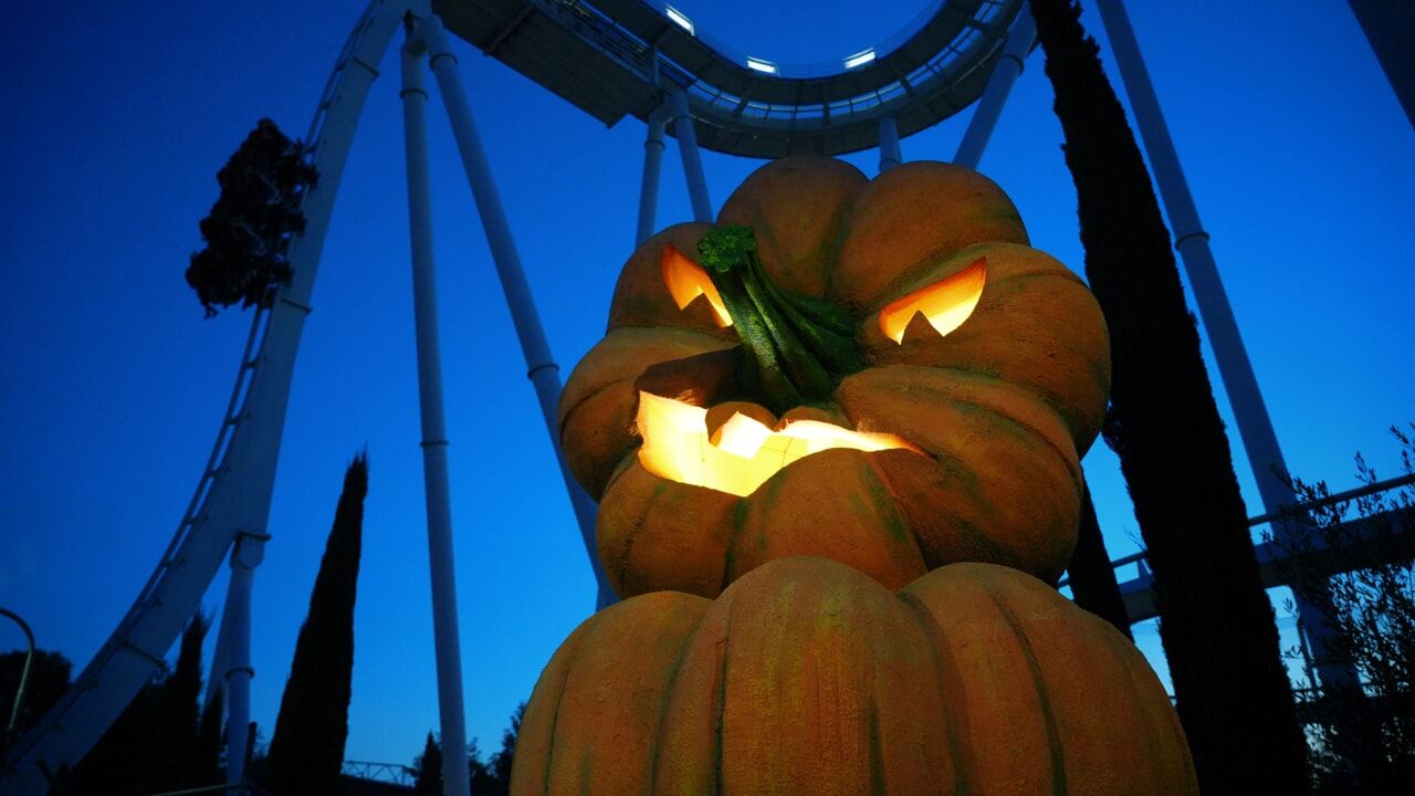 Zucca intagliata luminosa al crepuscolo, con le rotaie delle montagne russe che si stagliano sullo sfondo.