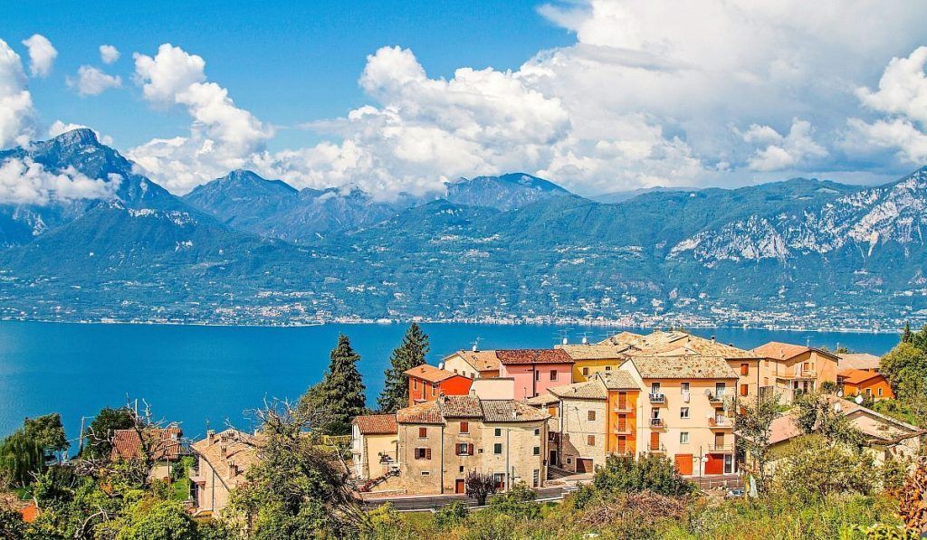 Villaggio pittoresco in riva al lago, con edifici dai tetti rossi, acqua azzurra e montagne sotto un cielo nuvoloso.