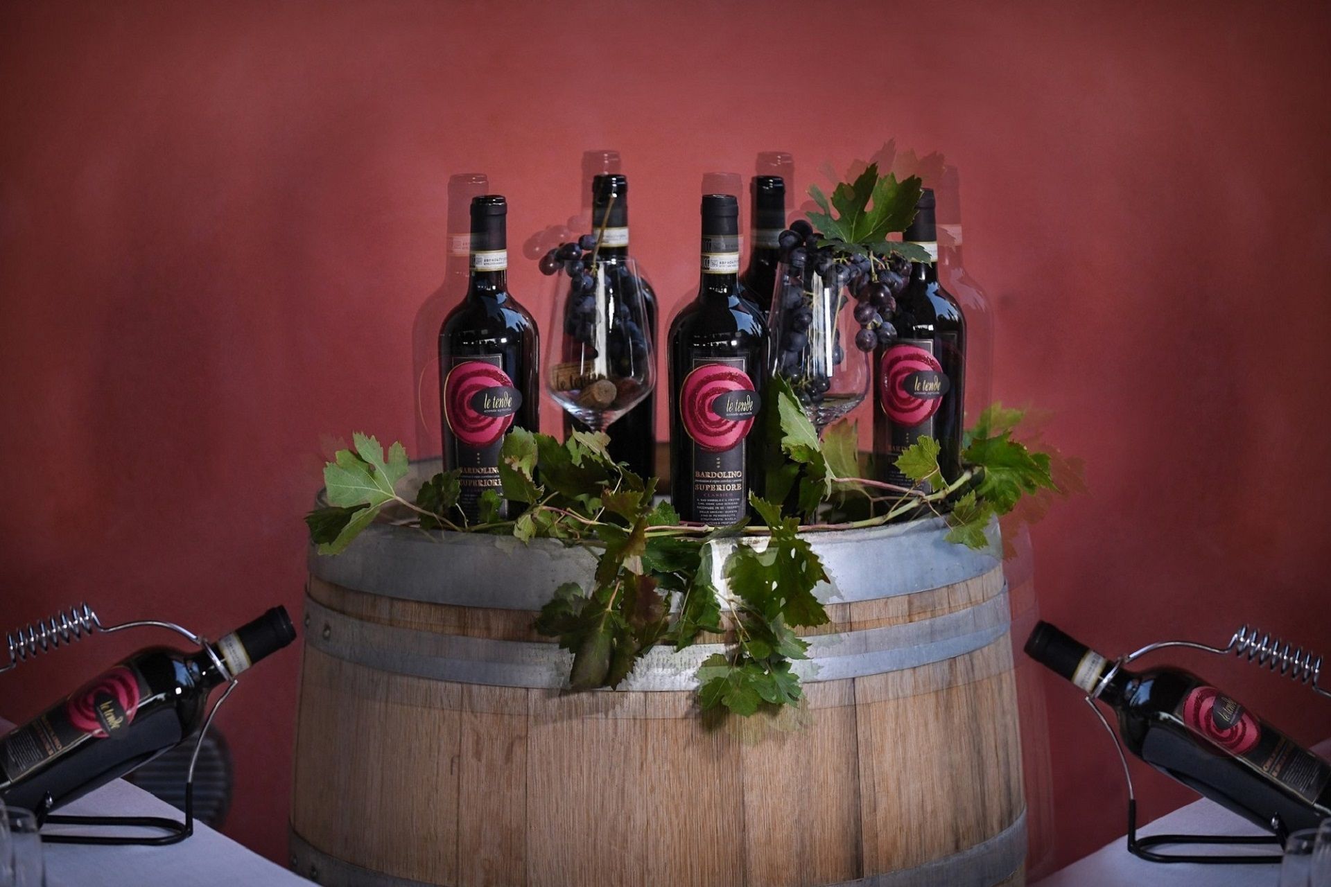 Bottiglie di vino disposte in un'esposizione a forma di botte di legno con fogliame verde su sfondo rosso