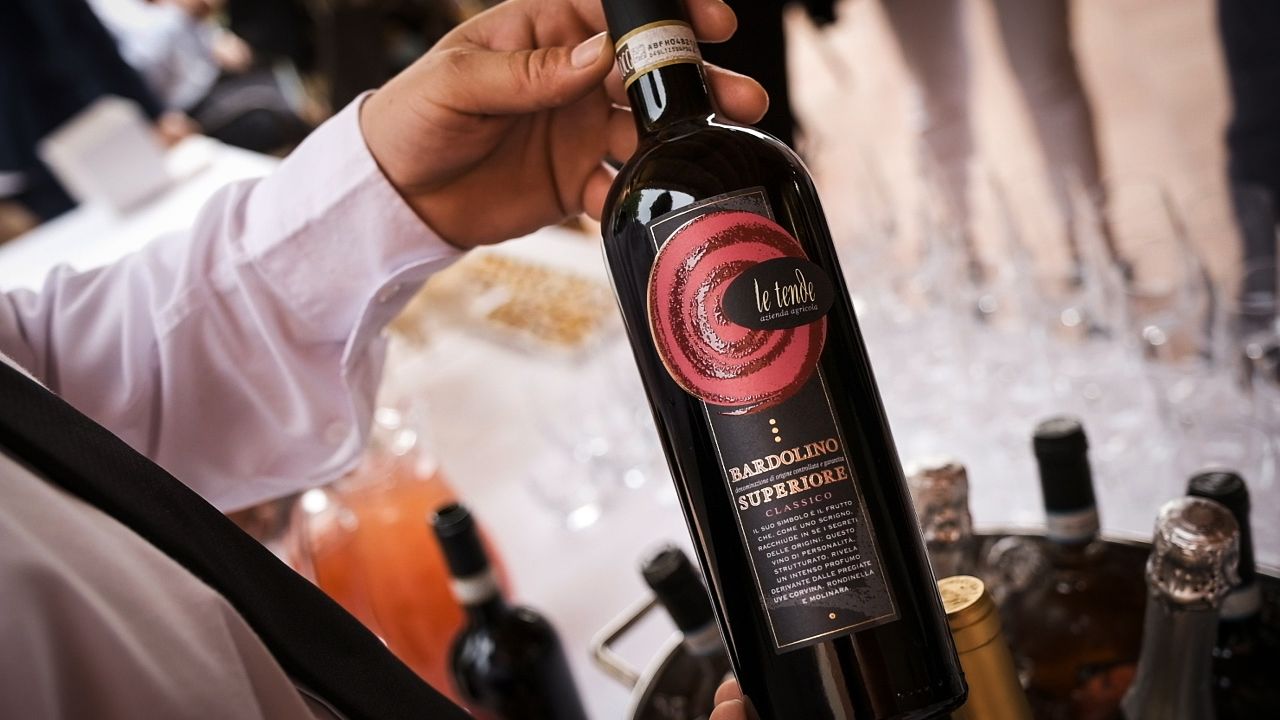 Mano che regge una bottiglia di vino rosso con etichetta rosa durante una degustazione.