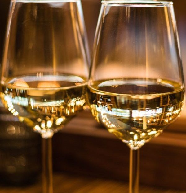 Due calici da vino trasparenti con vino bianco su un caldo bancone di legno.