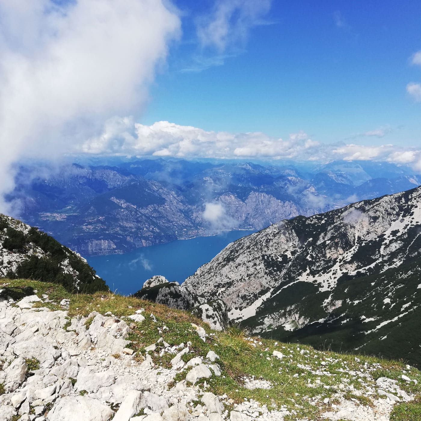 Un punto panoramico roccioso si affaccia su un lago blu sotto un cielo luminoso punteggiato di nuvole.