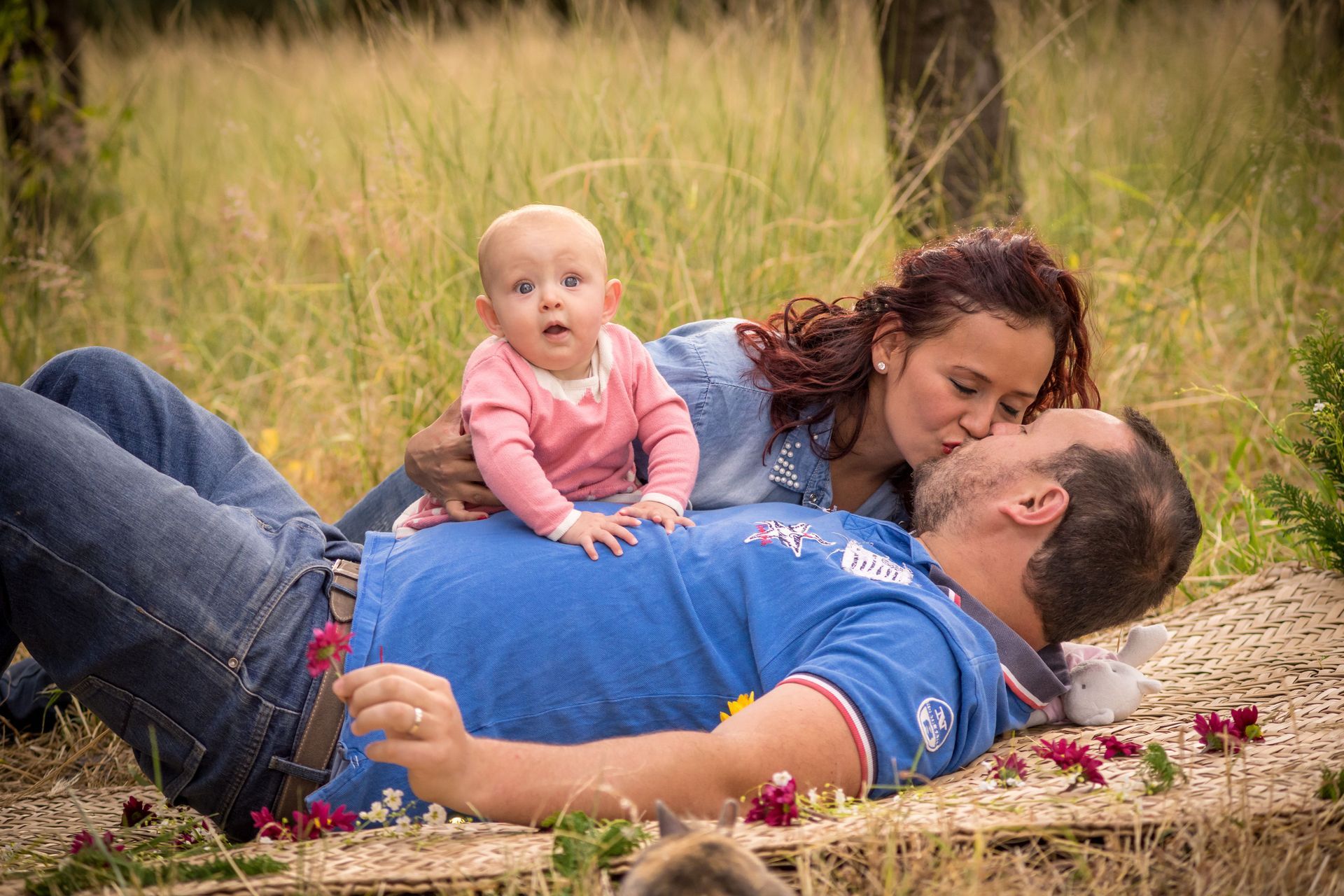 Una donna e un uomo sdraiati sull'erba con un bambino seduto sopra di loro, all'aperto.