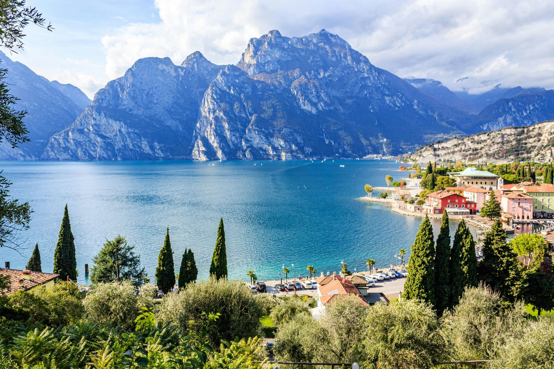 Cittadina lacustre affacciata su un lago turchese, con montagne e cipressi sotto un cielo azzurro brillante.
