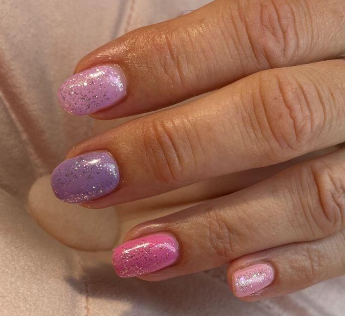 Een close-up van de nagels van een persoon met roze en paarse nagellak