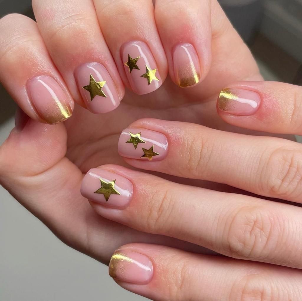 Een close-up van biab nagels van een vrouw met gouden sterren erop