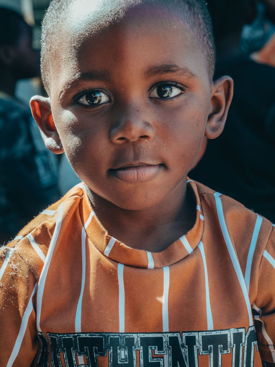 A woman is talking to a group of children sitting on the ground.
