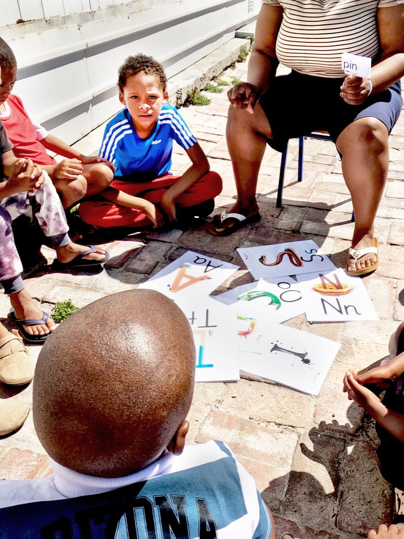 Kinderen leren buiten letters onder begeleiding van een volwassene. Gedrukte letters en tekeningen op de grond.