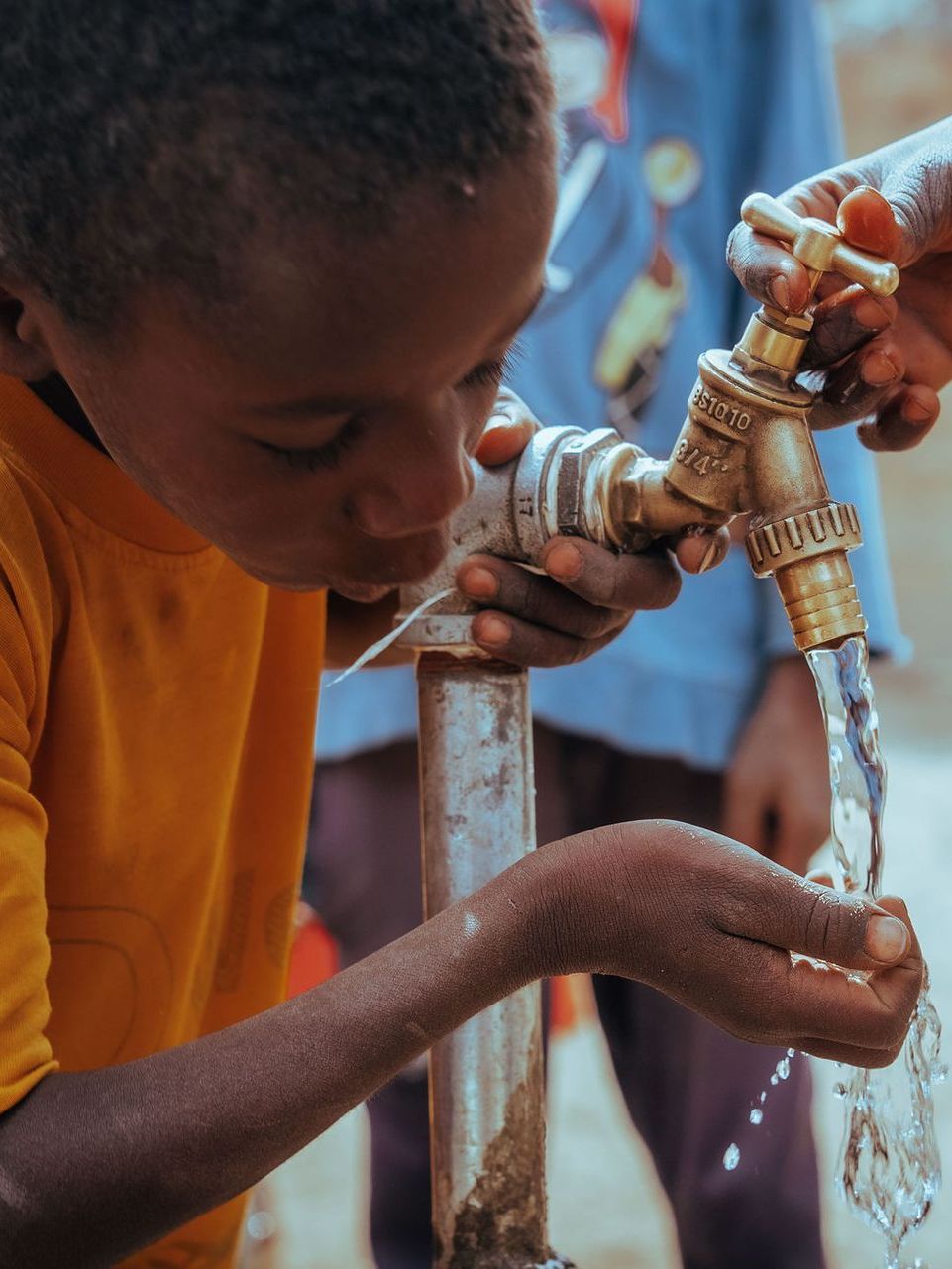 A young boy is drinking water from a faucet that says ' ethiopia ' on it