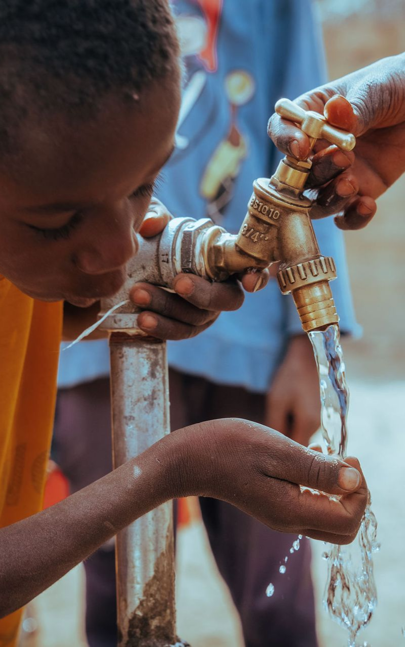 A woman is talking to a group of children sitting on the ground.