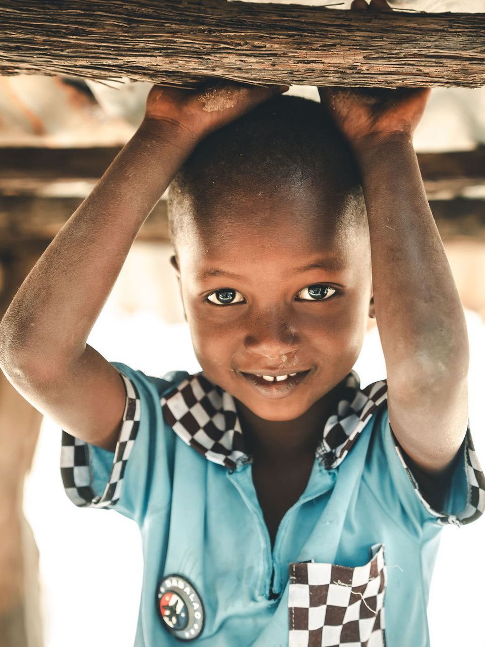 A young boy in a blue shirt is holding a log over his head.