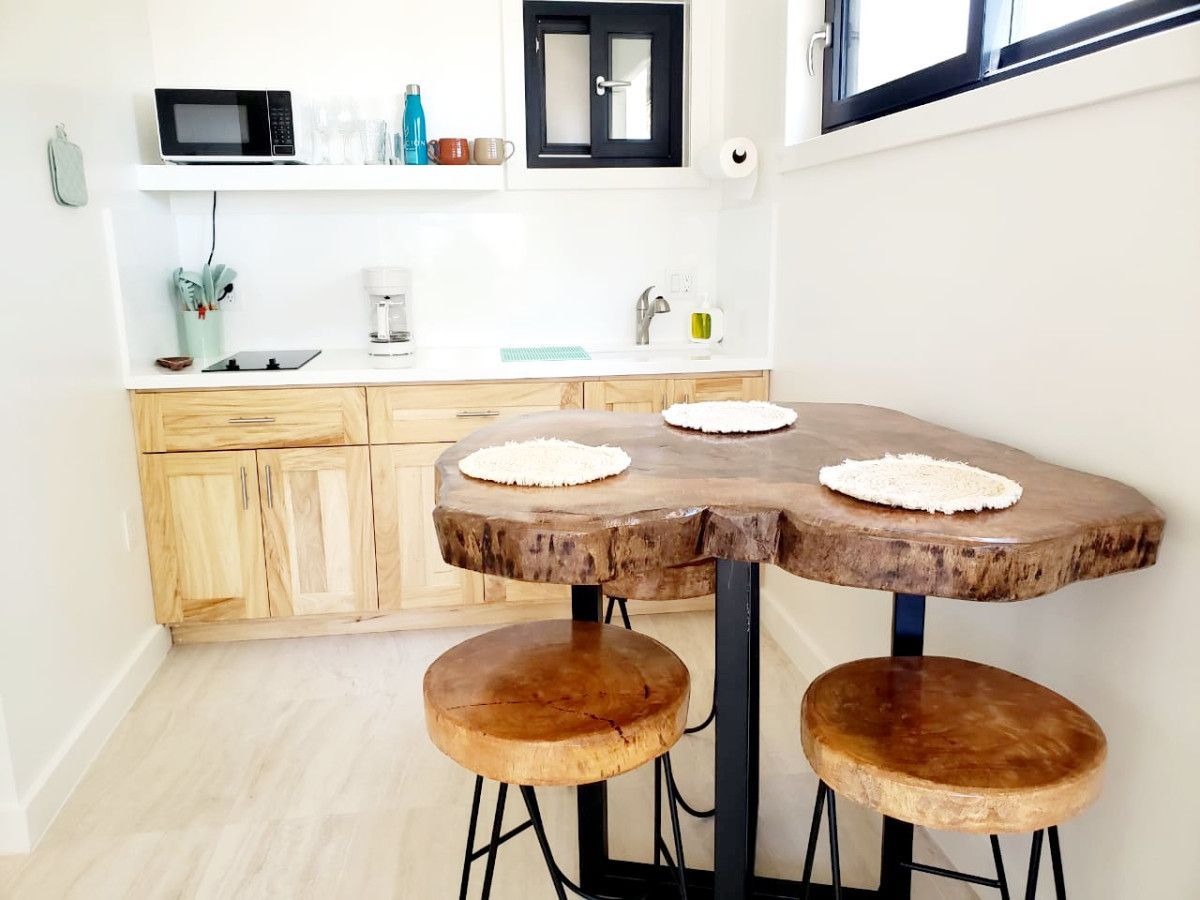 Kitchen with live-edge table and stools, microwave, and sink. White walls and light wood cabinets.