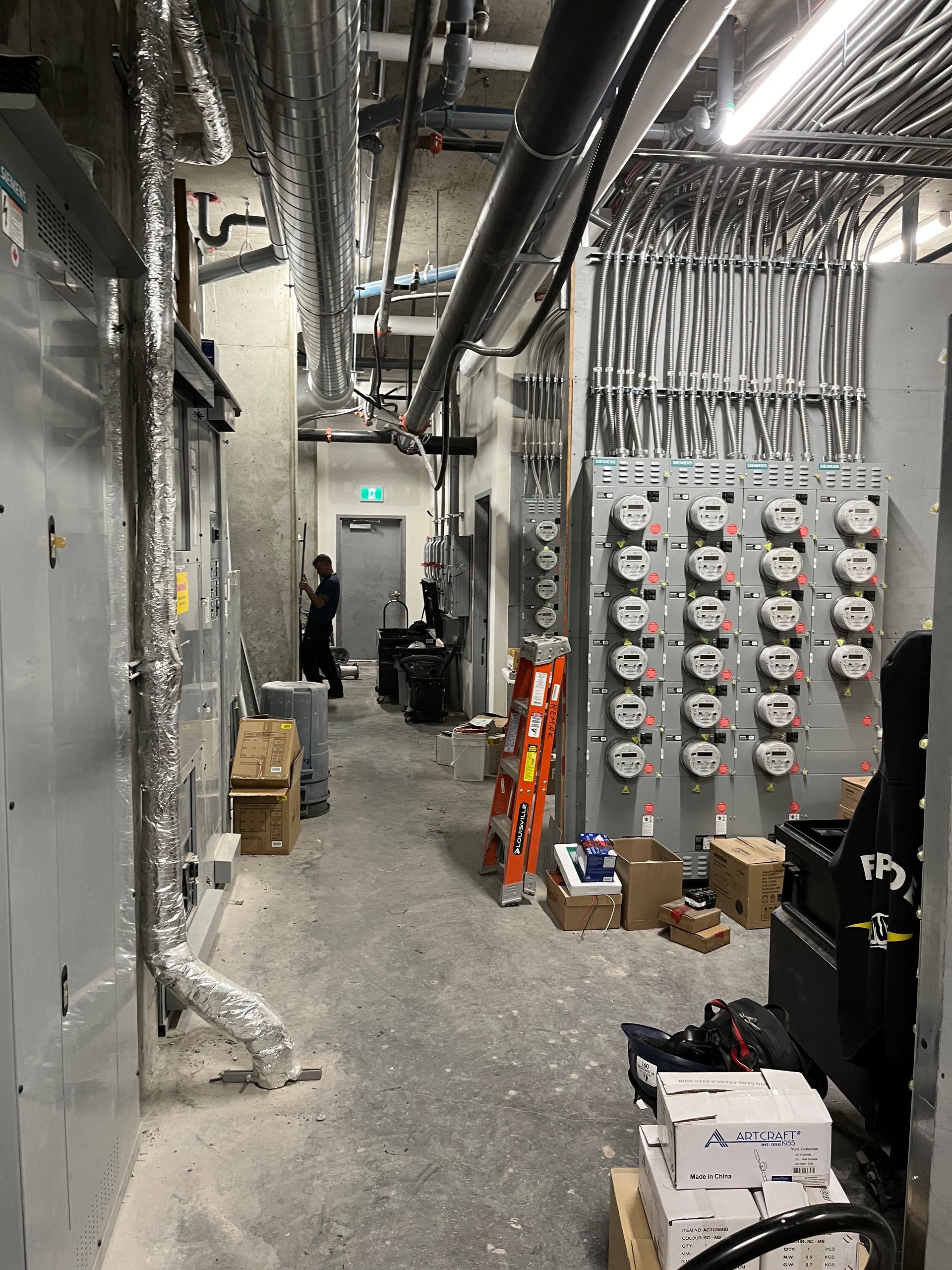 Un très long couloir avec beaucoup de tuyaux et de boîtes au sol.