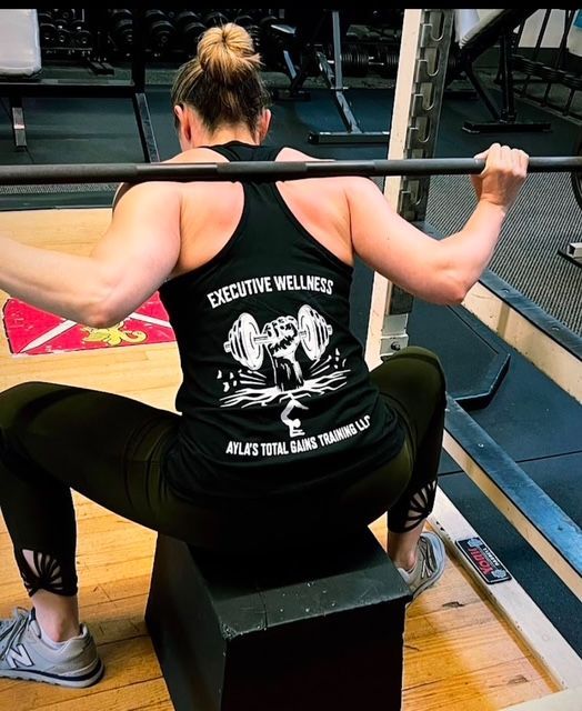 A woman squatting with a black tank top that says executive wellness