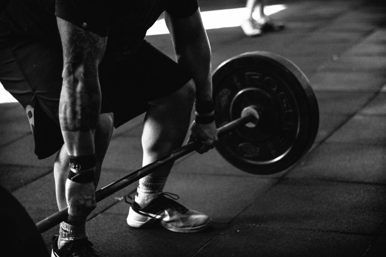 A man is lifting a barbell in a gym in a black and white photo.