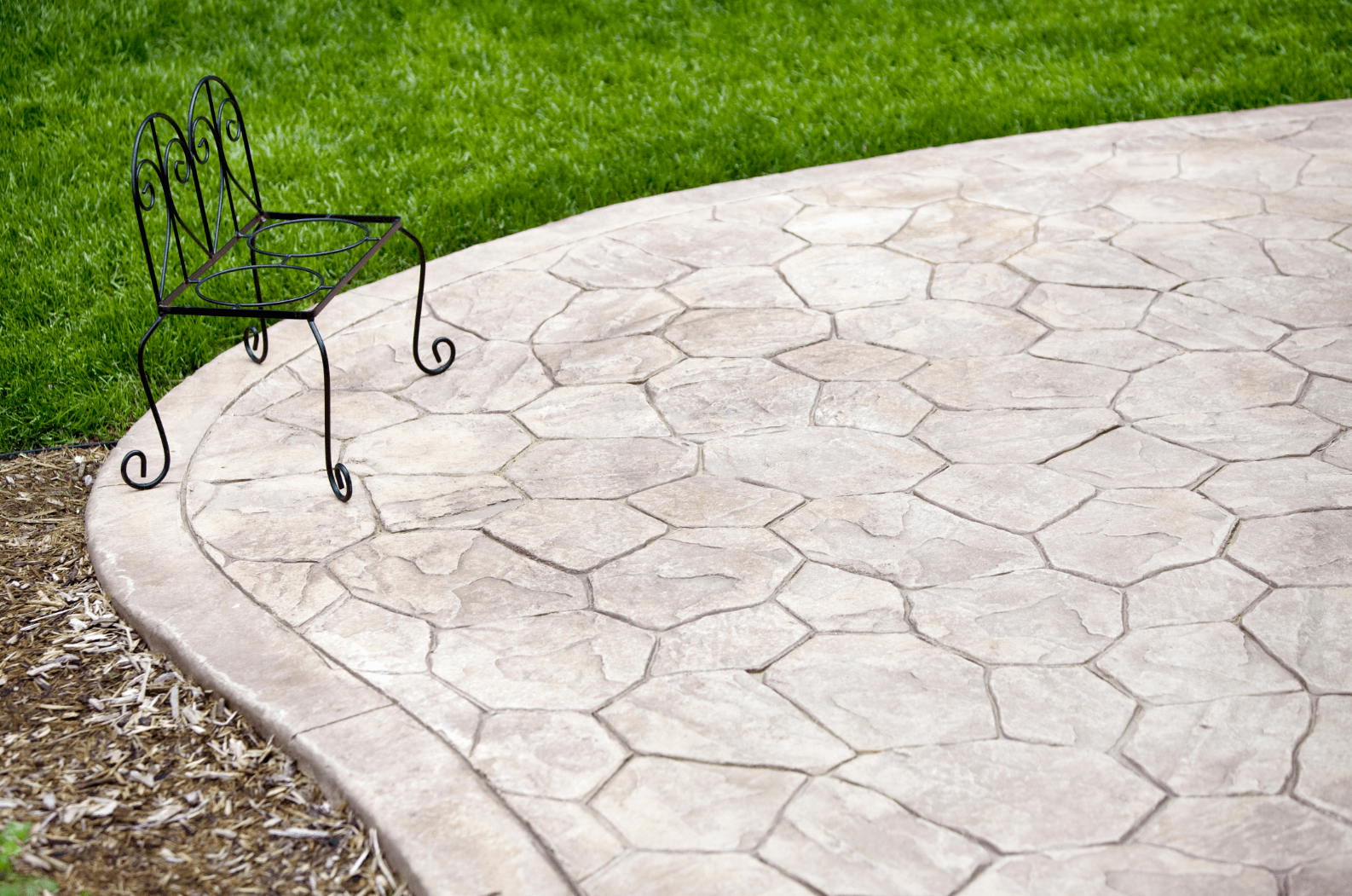 This is a picture of a stamped concrete patio at the edge of some lawn in a backyard.  The stamped concrete has an attractive circular border.