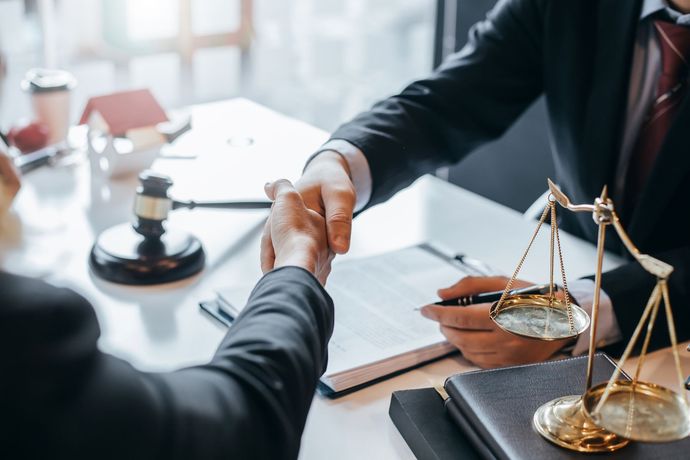 A lawyer is shaking hands with a client while sitting at a table.