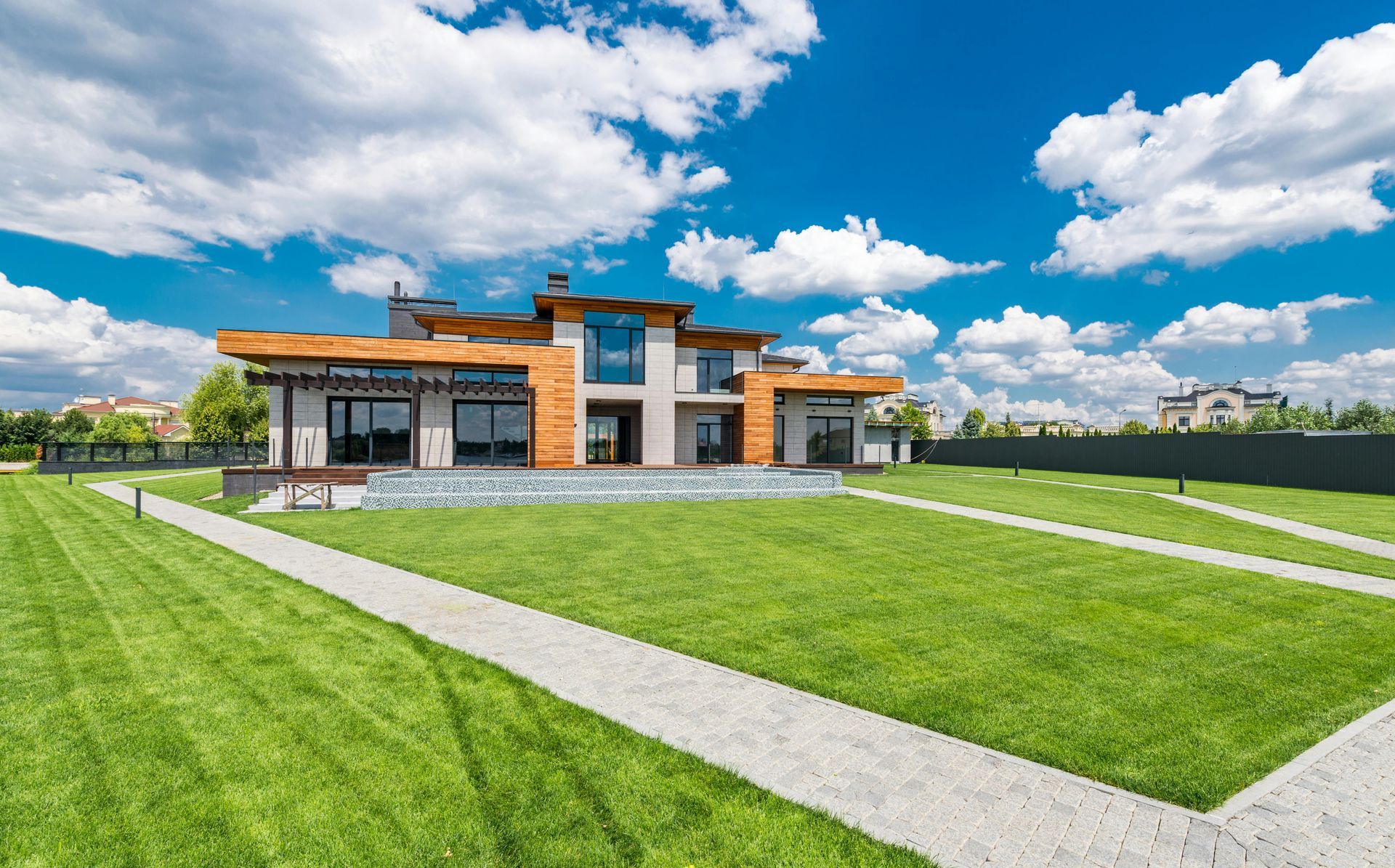 Modern house with a large green lawn under a bright blue sky with fluffy white clouds.