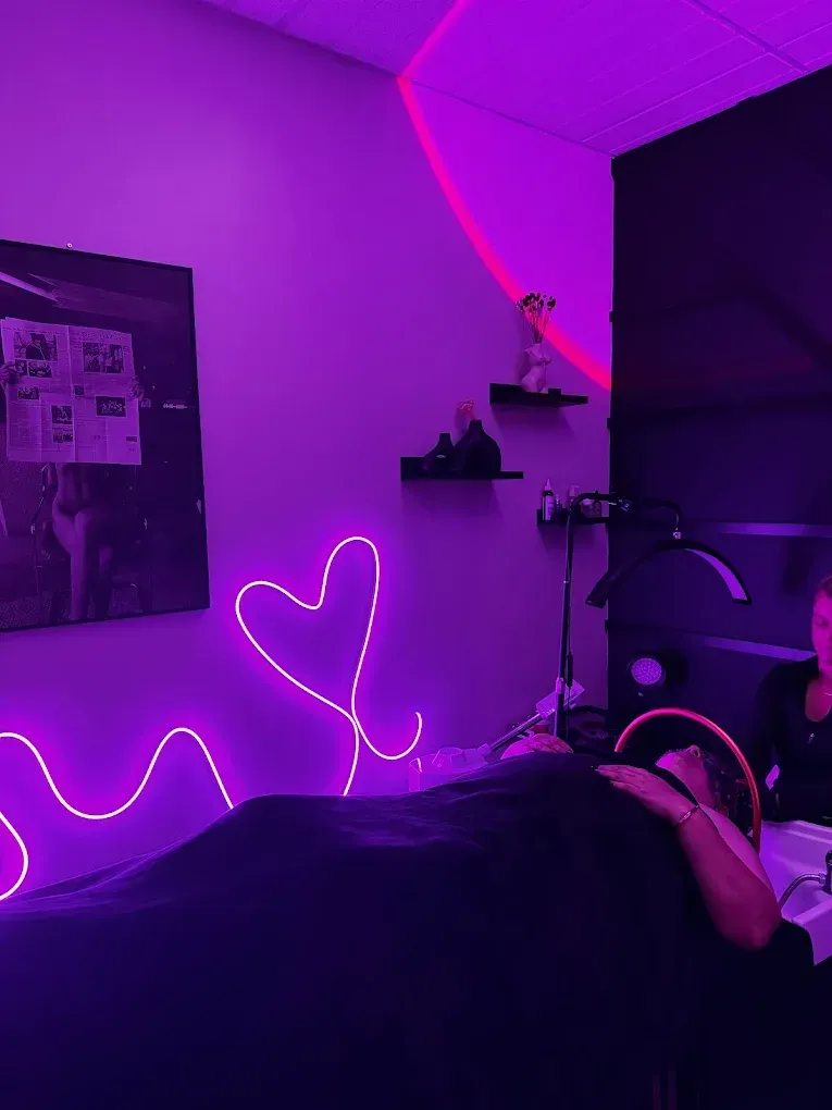 Person receiving beauty treatment in a room with purple neon heart and lighting.