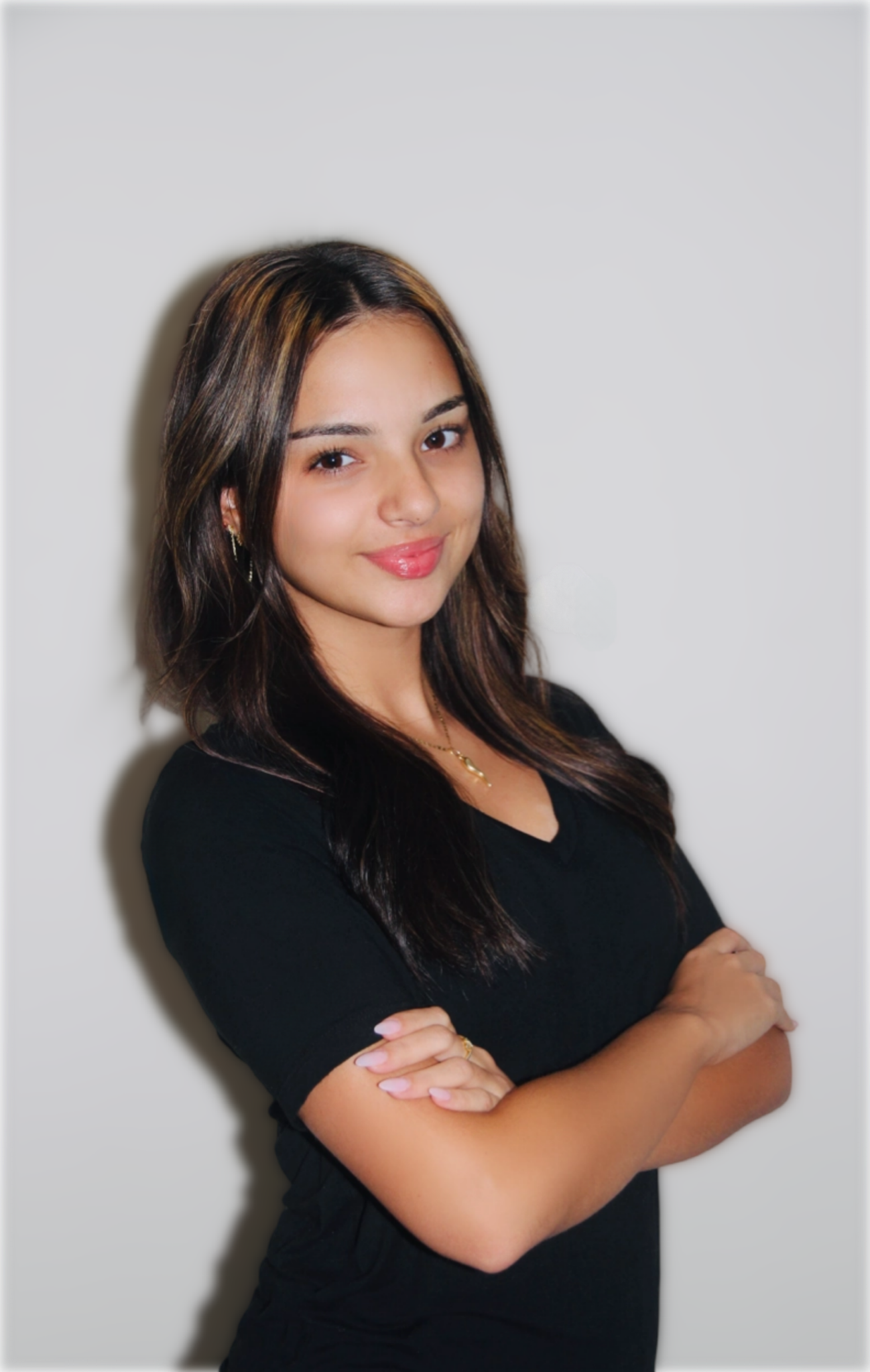 Young woman with crossed arms, smiling, wearing a black shirt, against a white background.