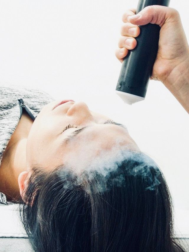 Person receiving scalp treatment with a device emitting vapor.