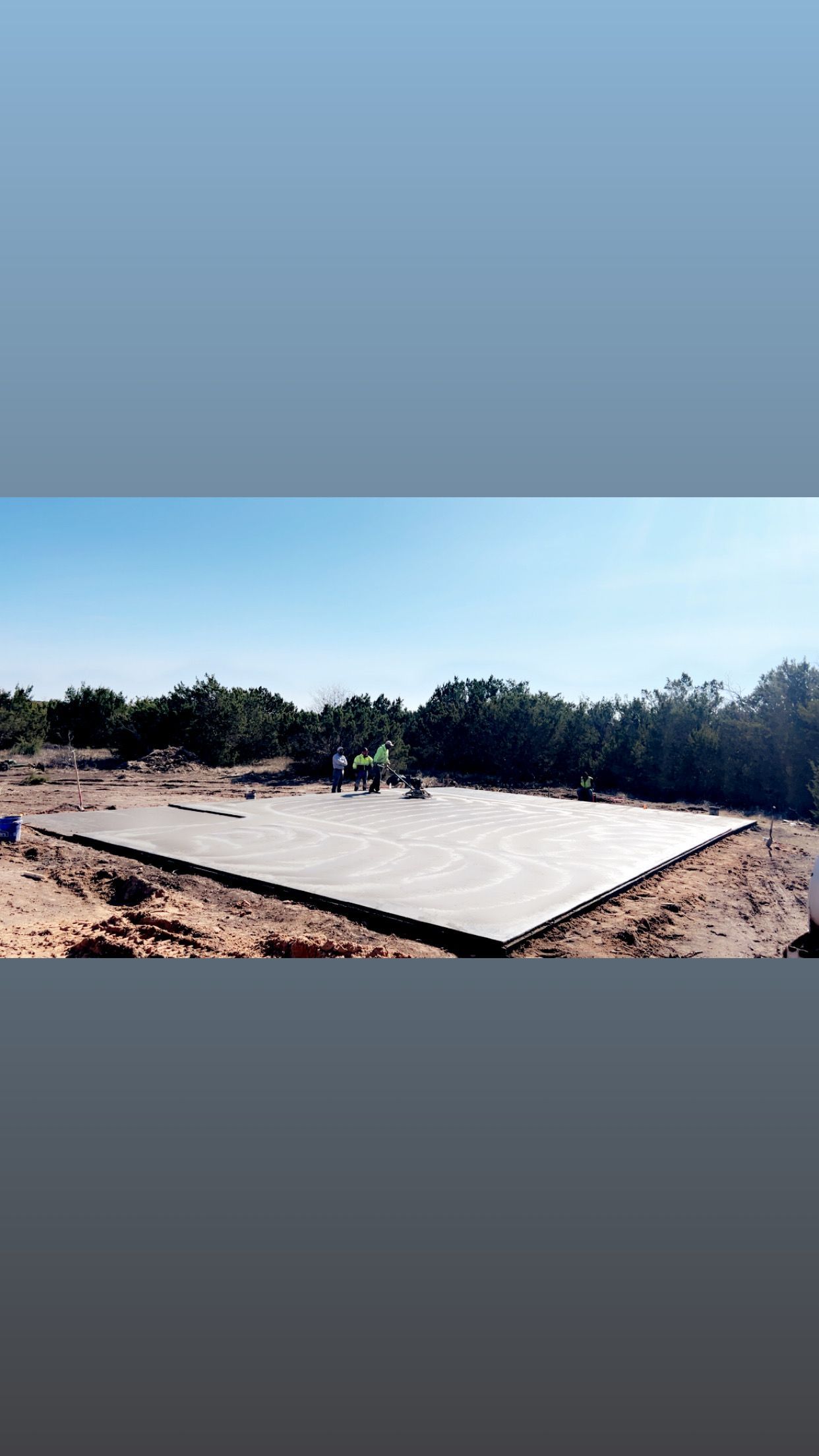 Concrete foundation slab surrounded by dirt, under a clear blue sky.