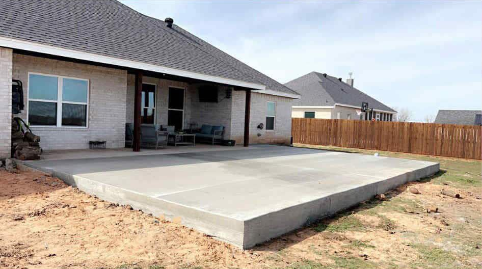 New concrete patio outside a light brick home, with covered porch and wooden fence in the background.