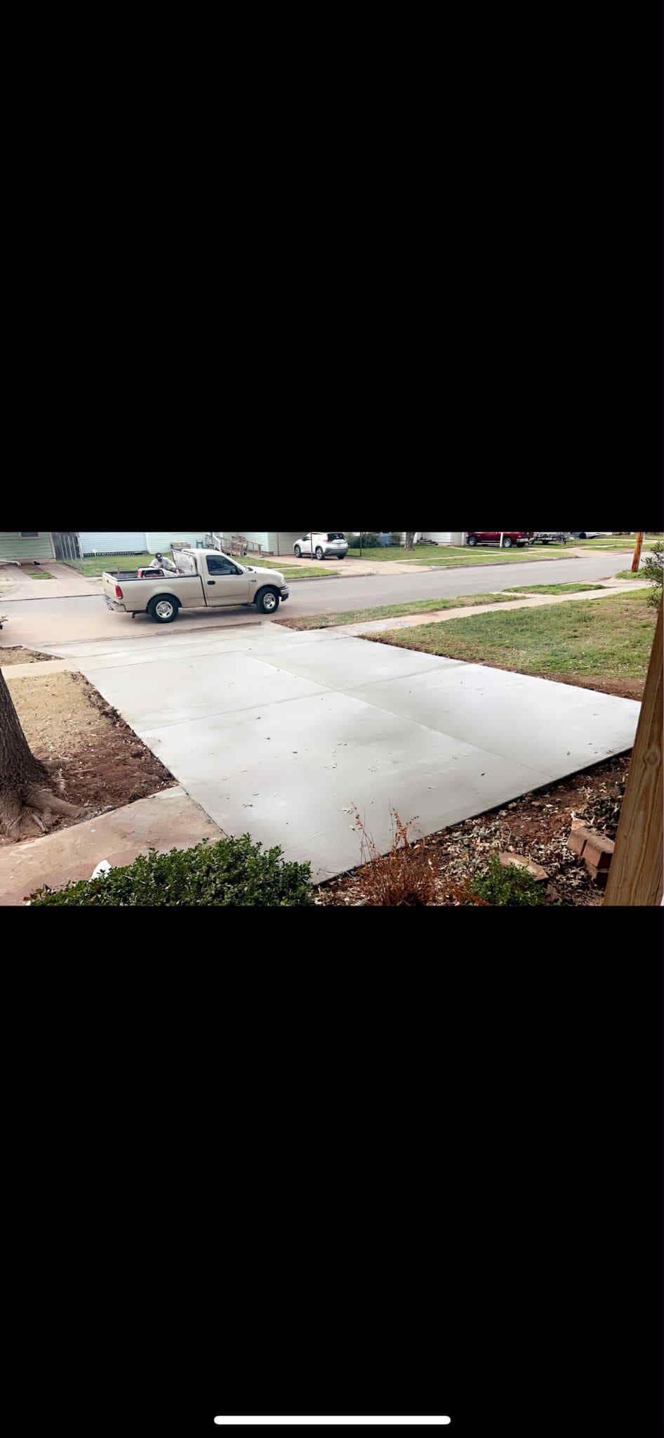 A light-colored pickup truck parked in a driveway. The concrete driveway leads to a street.