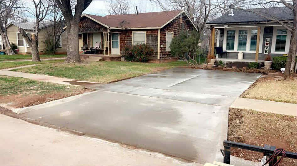 Man in orange shirt using squeegee on concrete driveway in front of a house.