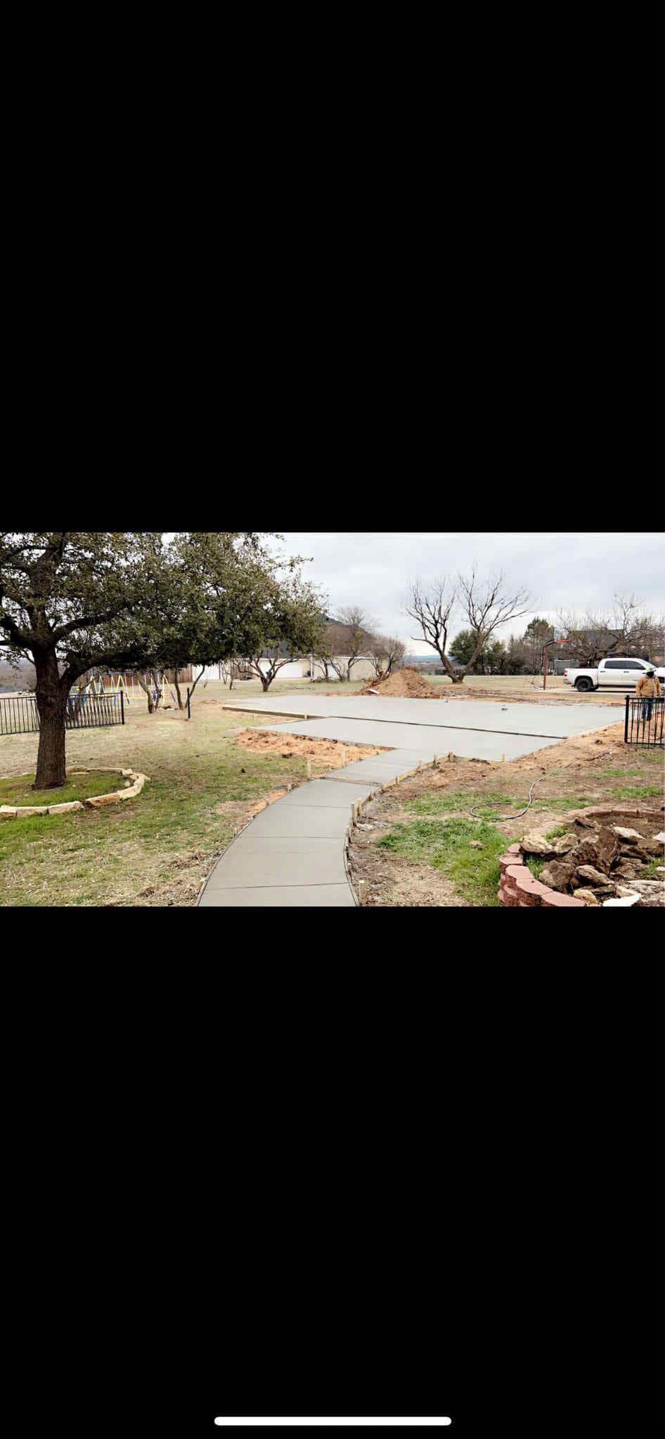 A curved paved walkway leads through a yard with a tree and scattered mulch on a cloudy day.