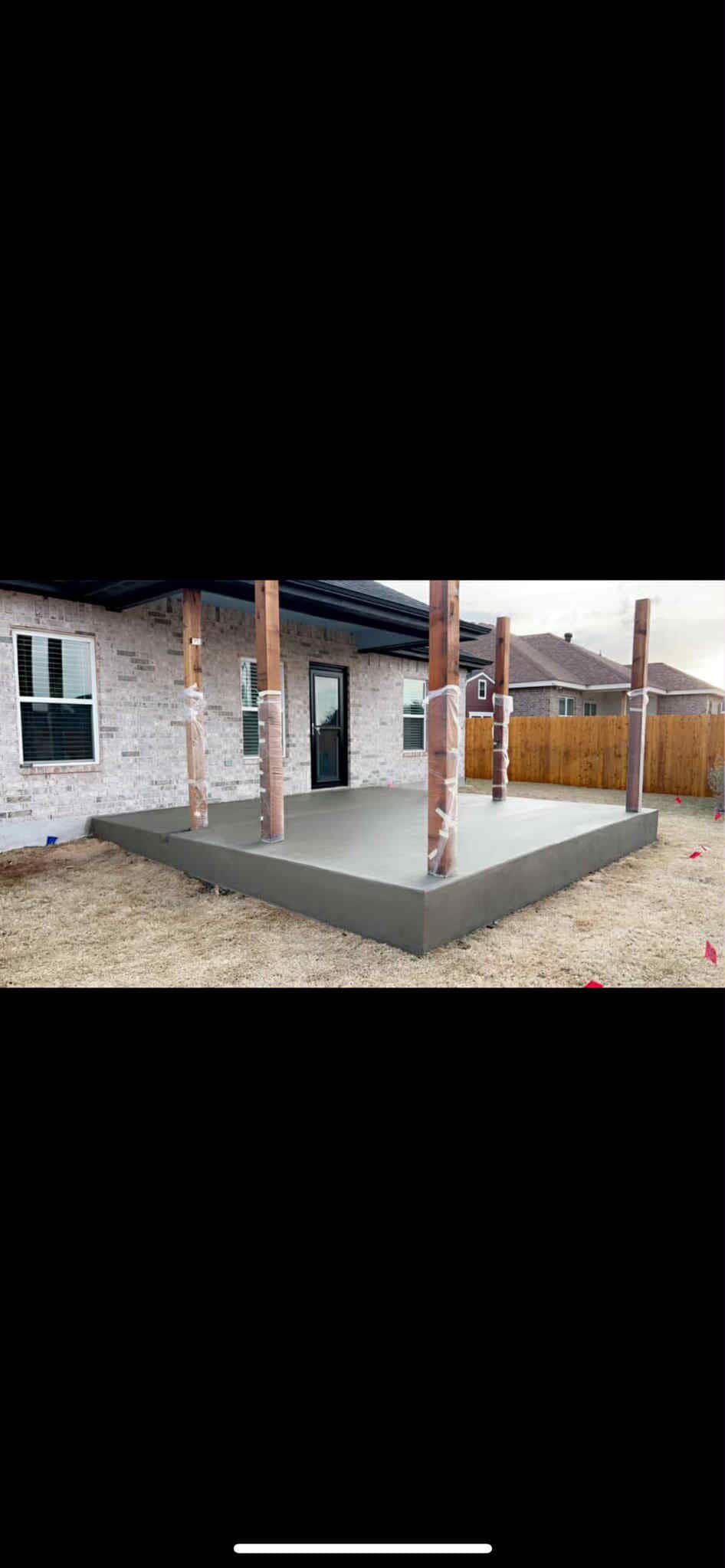 A concrete patio with wooden support beams is under construction next to a brick building.