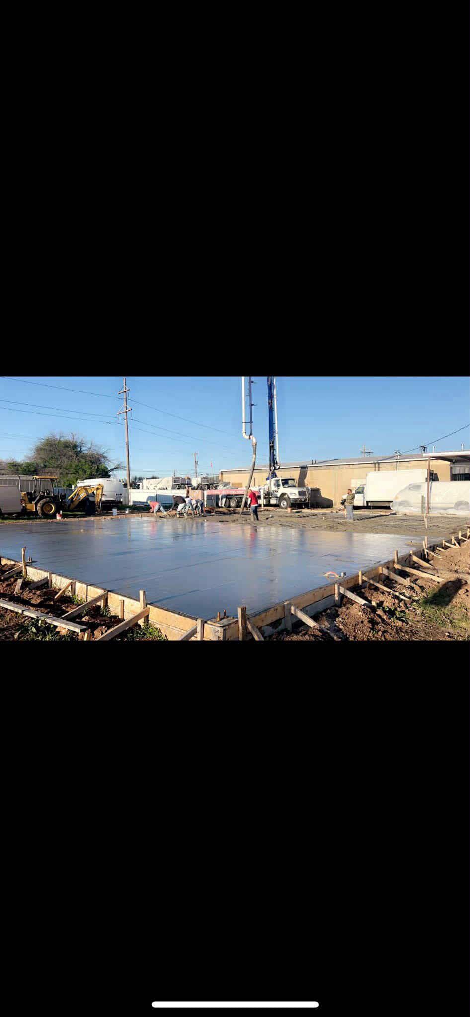 A body of water in a rural area with buildings and equipment visible in the background under a blue sky.