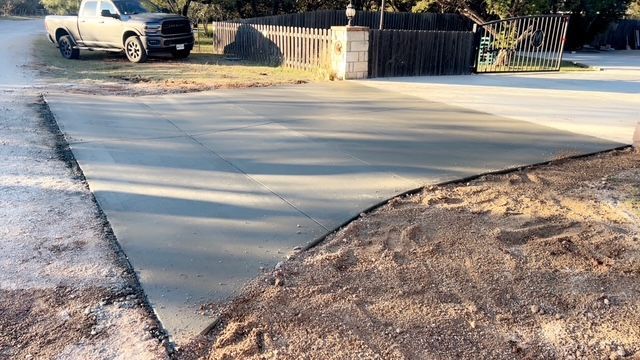 Curving concrete driveway in front of houses with green lawns and trees on a sunny day.