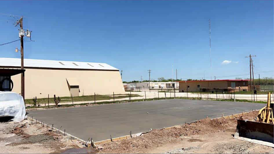 Newly poured concrete slab in an outdoor setting with buildings and blue sky in the background.