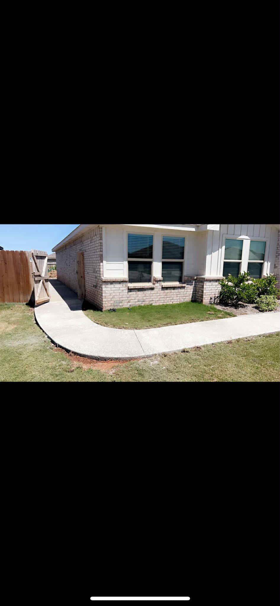 Stone patio with outdoor furniture, umbrella, and view of trees.