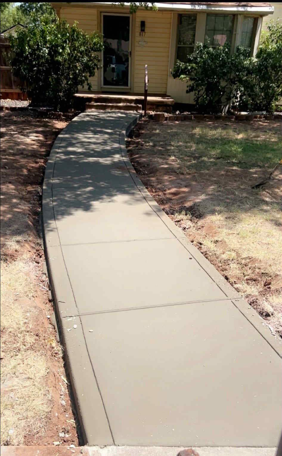 Person in jeans and work boots cleaning a large crack in a concrete walkway with a long-handled tool.
