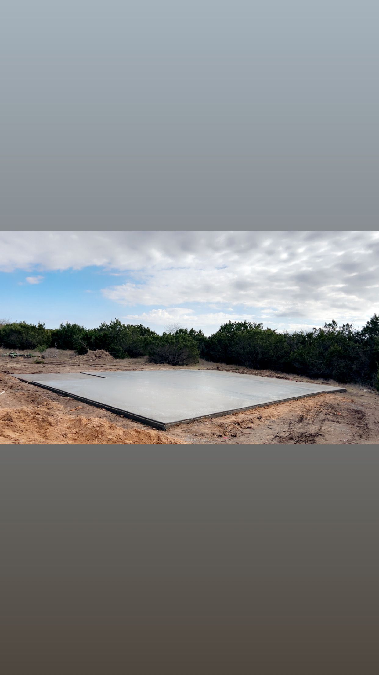 A constructed, flat concrete surface set in a dug-out area. Trees and sky are in the background.