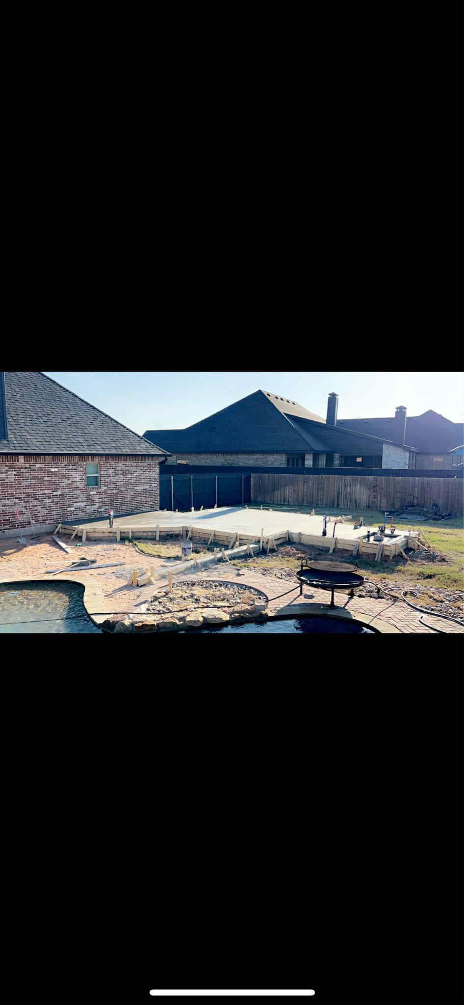 Backyard with construction. Houses and a dirt area, with a cement slab. Clear day.