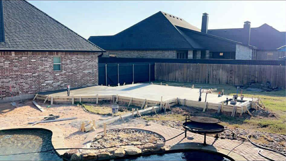 Concrete patio construction in a backyard, with forms in place, near a pool.