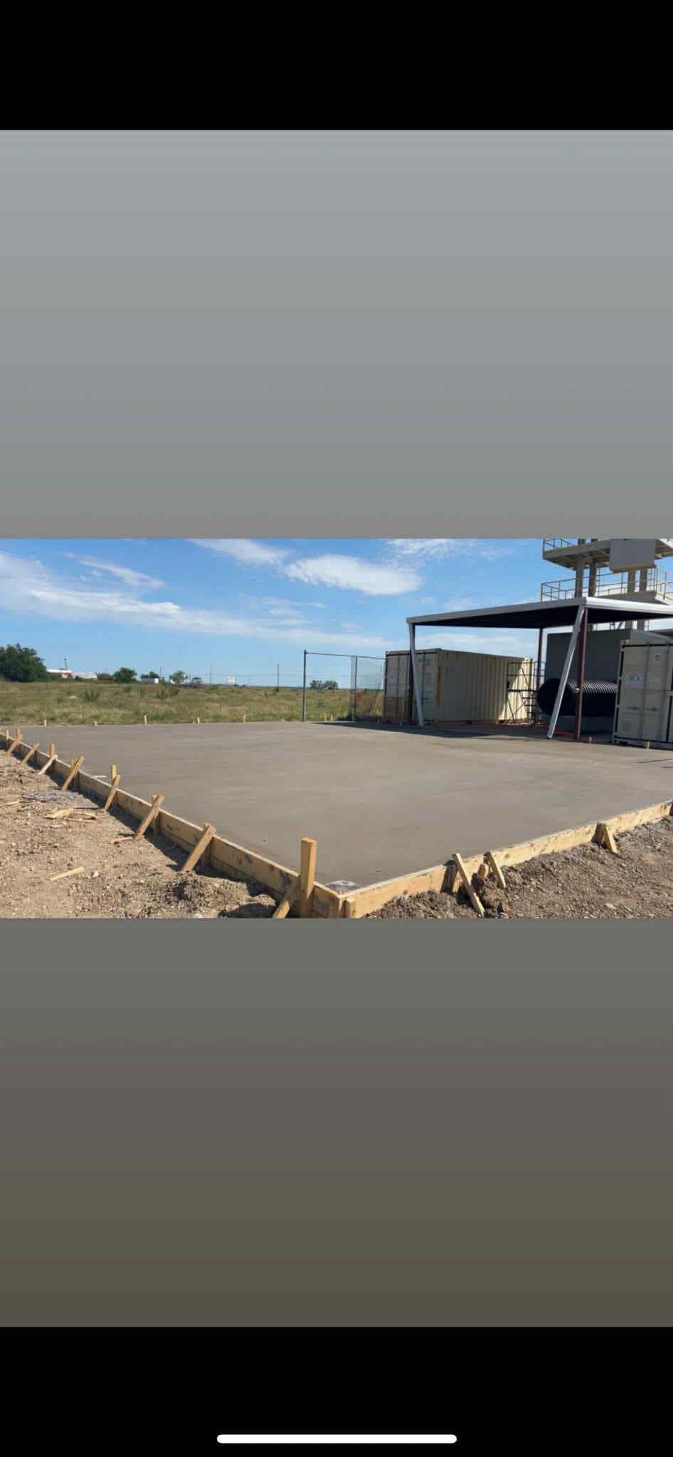 Construction site with concrete forms in foreground and unfinished concrete pad in open area, blue sky.
