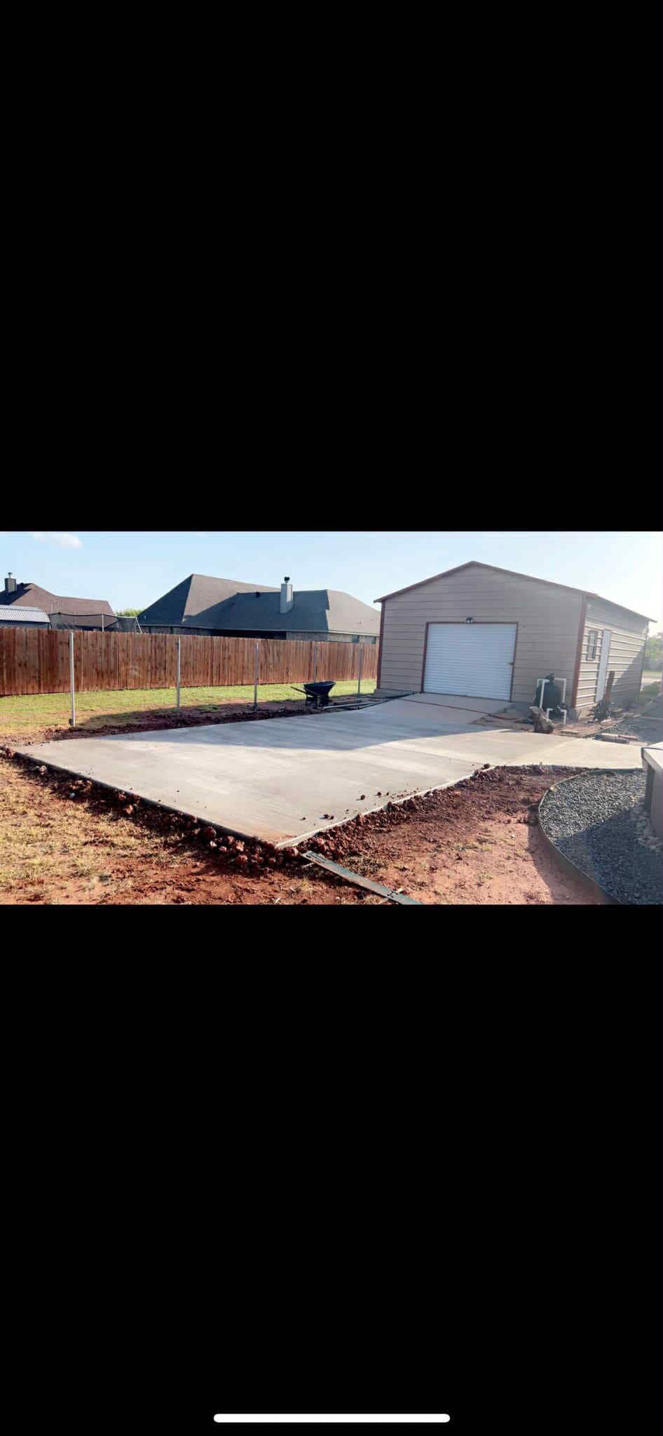Concrete foundation in front of a metal garage, dirt, and a wooden fence are in the background.