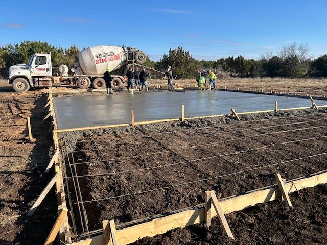 Construction site, concrete being poured for a foundation. Cement truck, workers, blue sky.