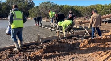 Concrete slab with rough edge, freshly poured on dirt. A building frame is in the background.