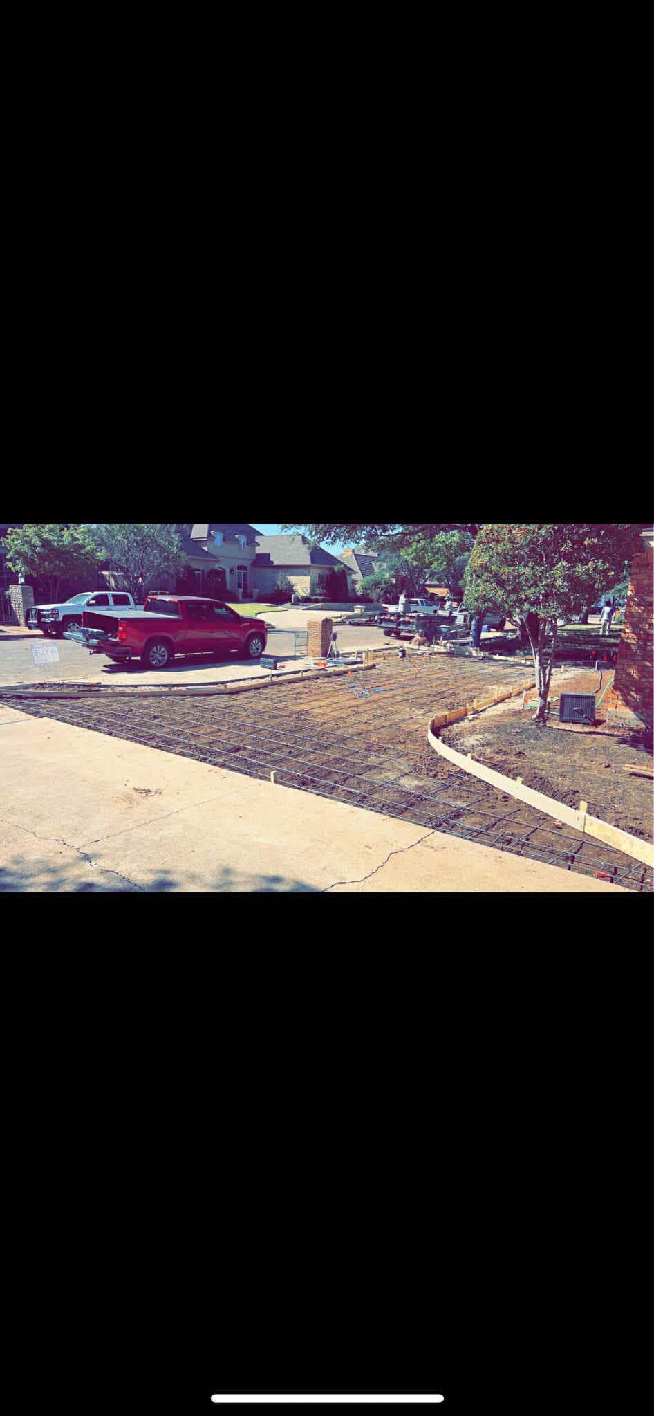 Construction worker power washing a wet parking lot, wearing an orange vest and hard hat. Sunny day.