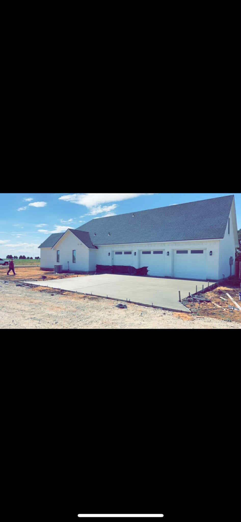 White building with dark gray roof, under construction, with a concrete driveway.